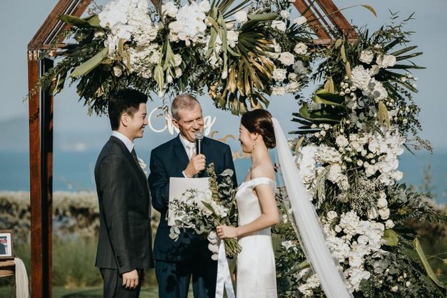 Peter Notley with a couple under a floral arch during a Phuket wedding